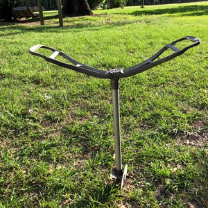 May include: A metal stand with two curved arms, designed for holding items. The stand is anchored to the ground with a metal spike.