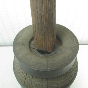 May include: A wooden spool with a metal band around the top. The spool is made of rough-hewn wood and has a natural brown color. The metal band is black and has a simple design.