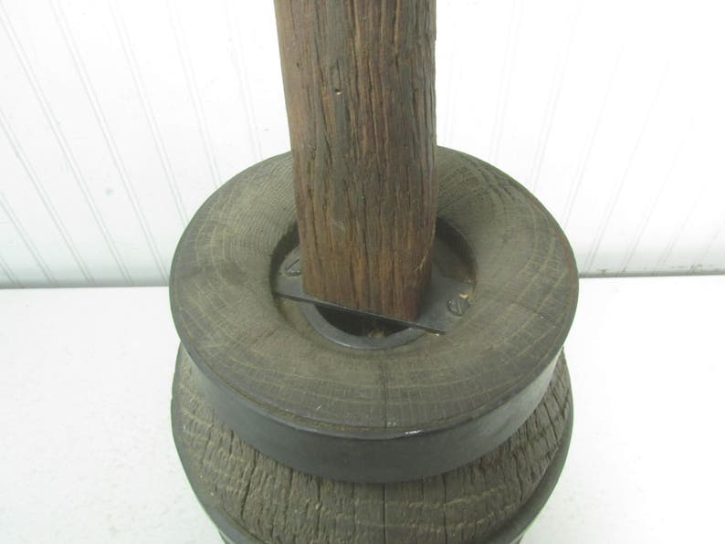 May include: A wooden spool with a metal band around the top. The spool is made of rough-hewn wood and has a natural brown color. The metal band is black and has a simple design.