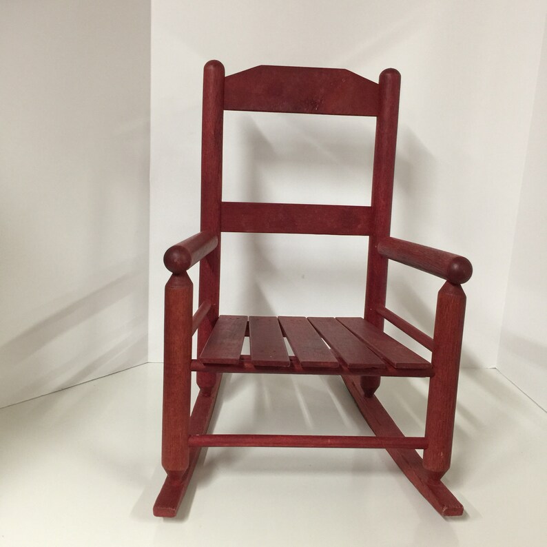 Puede incluir: Una silla mecedora de madera roja con un asiento de listones y apoyabrazos redondeados. La silla est&aacute; hecha de madera maciza y tiene un estilo r&uacute;stico, de granja.