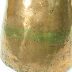 May include: A copper pitcher with a green band around the middle. The pitcher has a worn, aged look and is likely antique.