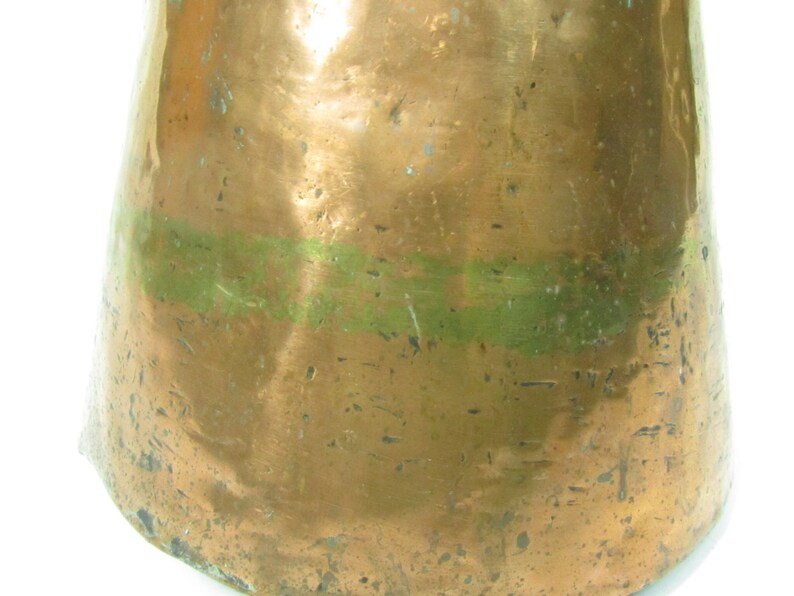 May include: A copper pitcher with a green band around the middle. The pitcher has a worn, aged look and is likely antique.