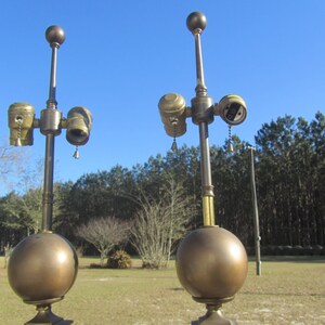 May include: Two antique brass table lamps with a round globe base and a single bulb socket. Each lamp has a pull chain switch and a decorative finial on top.