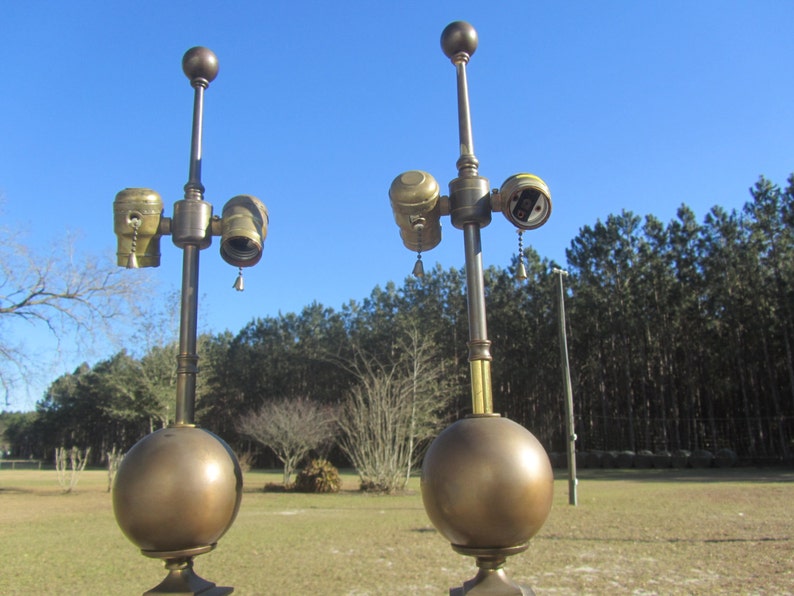 May include: Two antique brass table lamps with a round globe base and a single bulb socket. Each lamp has a pull chain switch and a decorative finial on top.