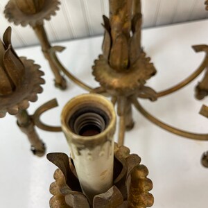 Pode incluir: Um candeeiro de teto de metal dourado com seis candelabros. Cada candeeiro tem uma base decorativa em forma de flor e uma tomada de porcelana branca.