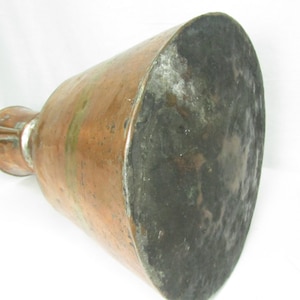 May include: A large copper pitcher with a wide base and a narrow neck. The pitcher has a worn, aged patina and a hammered texture.