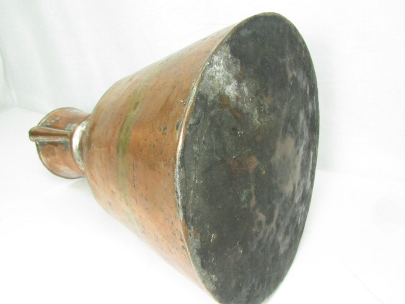 May include: A large copper pitcher with a wide base and a narrow neck. The pitcher has a worn, aged patina and a hammered texture.