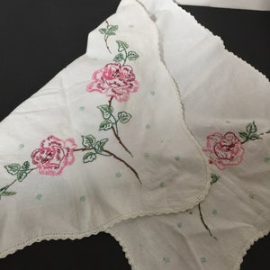 Op de afbeelding: Wit tafelkleed met een gegolfde rand en geborduurde roze rozen met groene bladeren.