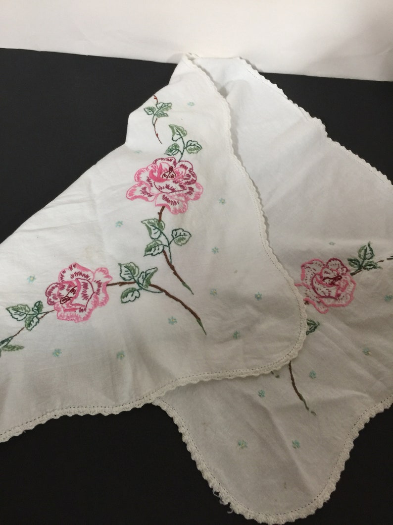 Op de afbeelding: Wit tafelkleed met een gegolfde rand en geborduurde roze rozen met groene bladeren.