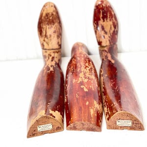 May include: Three wooden shoe forms with a red-brown finish. The forms are slightly worn and have a label on the bottom that reads "Bunting & Sons, London & Paris".