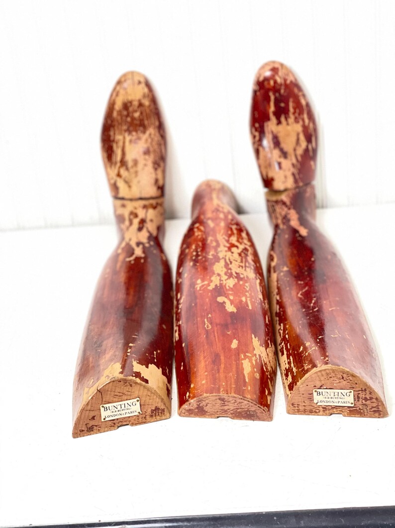 May include: Three wooden shoe forms with a red-brown finish. The forms are slightly worn and have a label on the bottom that reads "Bunting & Sons, London & Paris".