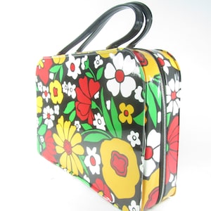 May include: A black vinyl handbag with a floral print featuring red, yellow, white, and green flowers. The bag has a top handle and a zipper closure.