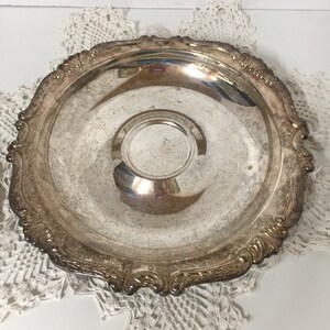 Puede incluir: Un plato de servir de plata con un borde decorativo y adornado. El plato es redondo y tiene un centro ligeramente elevado.