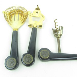 Op de afbeelding: Een set van drie gouden bargereedschappen met zwarte kunststof handvatten. De gereedschappen omvatten een cocktailscheider, een flesopener en een kurkentrekker.