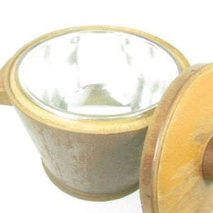 May include: A vintage ice bucket with a clear glass insert and a wooden exterior. The wooden lid is partially open, revealing the interior. The bucket has a handle on one side and a light brown finish.