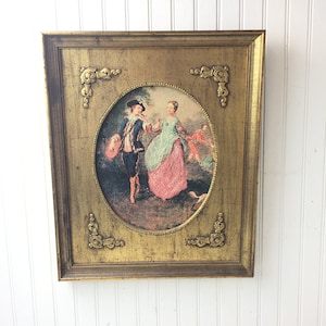 May include: A framed oval print of a couple in 18th century clothing, set against a gold background with ornate corners. The man is wearing a blue coat and hat, and the woman is wearing a pink and green dress.