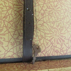 May include: A close-up of a brown leather strap with a metal buckle. The strap is attached to a surface with a patterned design.