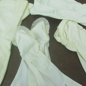 May include: Four pairs of white, long, elbow-length gloves. The gloves are made of a soft, stretchy fabric and have a delicate, ruffled trim at the wrist.