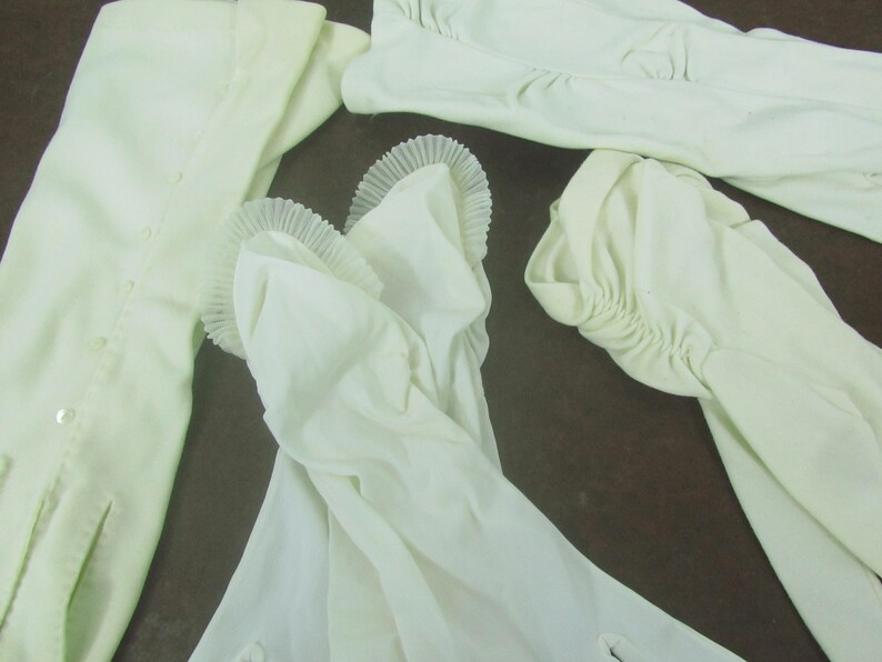 May include: Four pairs of white, long, elbow-length gloves. The gloves are made of a soft, stretchy fabric and have a delicate, ruffled trim at the wrist.
