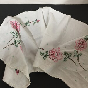Op de afbeelding: Witte tafelrunner met roze en groene geborduurde rozen. De runner heeft een gegolfde rand.