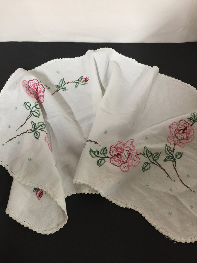 Op de afbeelding: Witte tafelrunner met roze en groene geborduurde rozen. De runner heeft een gegolfde rand.