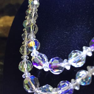 May include: A multi-strand iridescent crystal necklace with faceted beads. The necklace is made of clear glass beads with a rainbow sheen.