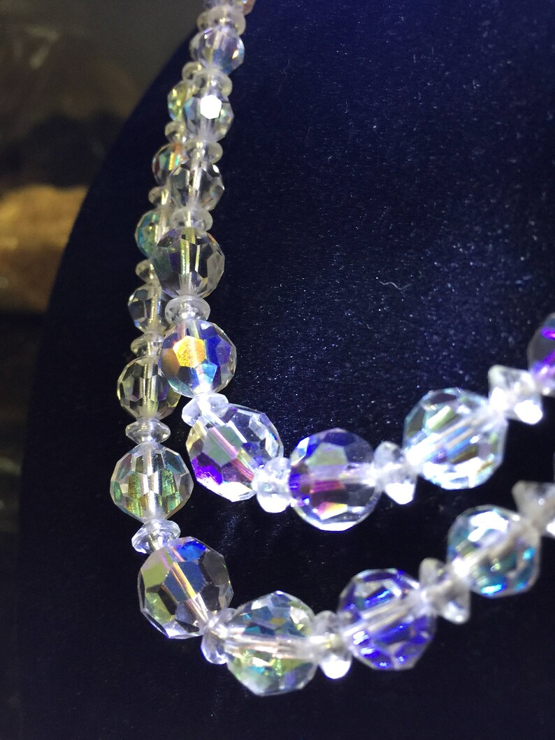 May include: A multi-strand iridescent crystal necklace with faceted beads. The necklace is made of clear glass beads with a rainbow sheen.