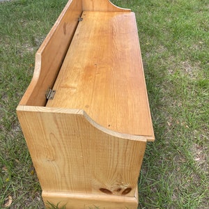 K&ouml;nnte beinhalten: Eine Holz-Aufbewahrungsbank mit einer Klappdeckel. Die Bank ist aus hellem Holz und hat ein schlichtes Design.