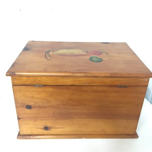 May include: A wooden storage box with a hinged lid. The lid is painted with a duck design in shades of green, yellow, and brown. The box is made of natural wood with a light brown finish.