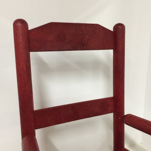 Puede incluir: Una silla de madera roja con respaldo alto y dise&ntilde;o sencillo. La silla tiene un acabado ligeramente desgastado, lo que le da un aspecto r&uacute;stico.
