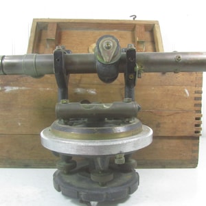 May include: Antique brass theodolite surveying instrument with a wooden box. The theodolite has a telescope, a level, and a graduated circle.