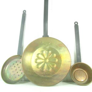 May include: Three vintage copper kitchen utensils with black handles. The largest utensil is a round pan with a floral design. The other two utensils are a ladle and a slotted spoon.