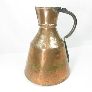 May include: A vintage copper pitcher with a hammered finish and a dark metal handle. The pitcher has a wide base and a narrow neck.