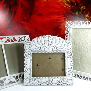 May include: Three white picture frames with ornate designs. The frames are made of wood and have a distressed white finish. The frames are all different sizes and shapes.
