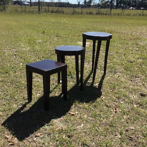 May include: Three dark brown wooden nesting tables with rounded edges and a simple design. The tables are arranged in order of size, with the largest table in the back and the smallest table in the front.