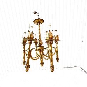 Pode incluir: Um candeeiro de teto de metal dourado com seis luzes. O candeeiro de teto tem um design floral com um caule central e seis bra&ccedil;os que se curvam para fora. Cada bra&ccedil;o tem um acess&oacute;rio de luz com uma l&acirc;mpada de vidro transparente. O candeeiro de teto est&aacute; pendurado num teto branco.