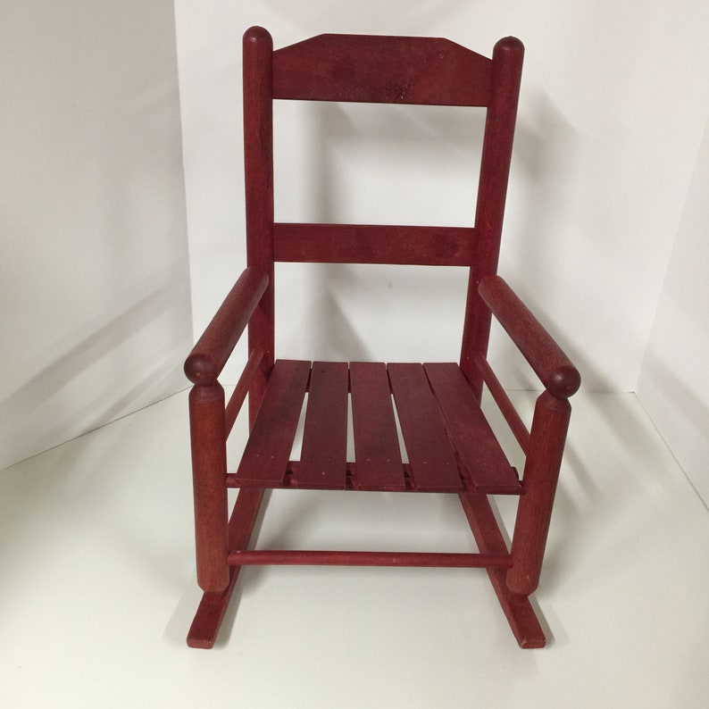 Puede incluir: Una silla mecedora de madera roja con un asiento de listones y apoyabrazos redondeados. La silla est&aacute; hecha de madera maciza y tiene un estilo r&uacute;stico, de granja.