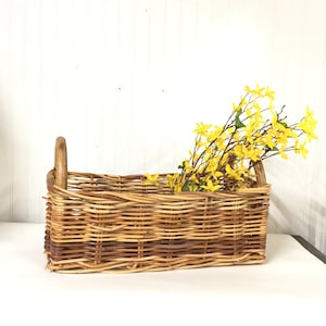 May include: A rectangular wicker basket with a brown handle, filled with yellow flowers. The basket is made of woven natural materials and has a rustic, farmhouse style.