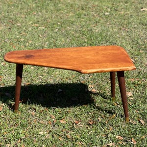 May include: A mid-century modern coffee table with a unique, asymmetrical, wood top and four legs with brass tips. The table is made of solid wood and has a rich, warm brown color.