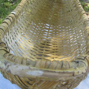 May include: A large, woven basket made of natural, light brown bamboo. The basket is oval shaped and has a wide, open top. The basket is empty and appears to be handmade.