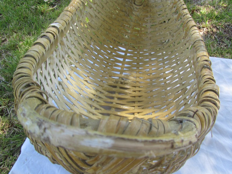 May include: A large, woven basket made of natural, light brown bamboo. The basket is oval shaped and has a wide, open top. The basket is empty and appears to be handmade.
