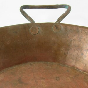 May include: A large, round copper pan with a single handle. The pan has a hammered finish and shows signs of age and use.