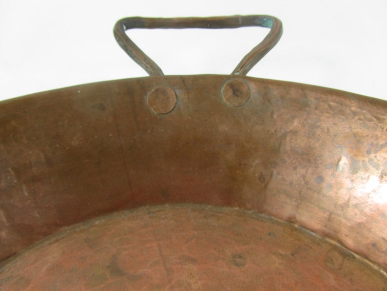 May include: A large, round copper pan with a single handle. The pan has a hammered finish and shows signs of age and use.
