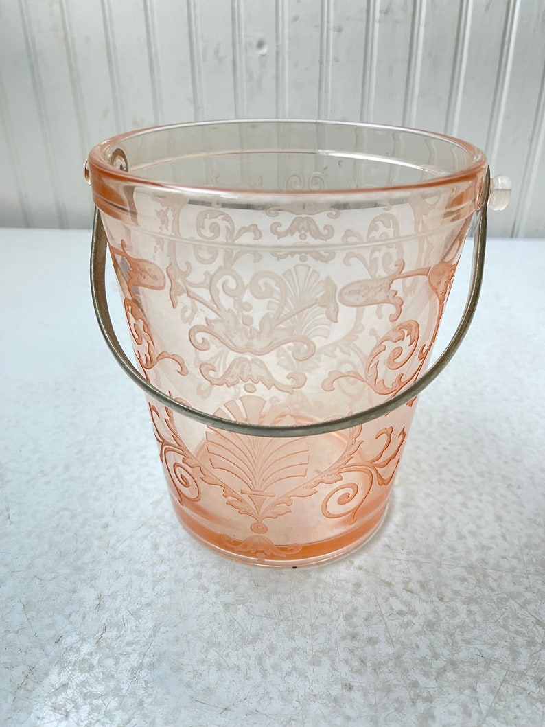 May include: A pink glass ice bucket with a silver handle and a delicate floral pattern.
