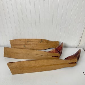 May include: Three wooden shoe forms, two are light brown and one is a darker brown with red paint. The forms are curved and have a rounded end.
