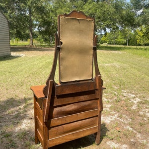 May include: Antique wooden vanity with a beveled mirror and three drawers. The vanity is made of dark wood and has a simple design.