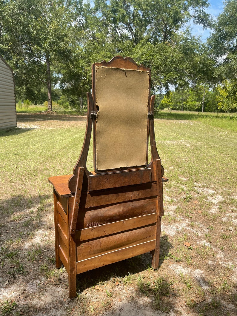 May include: Antique wooden vanity with a beveled mirror and three drawers. The vanity is made of dark wood and has a simple design.