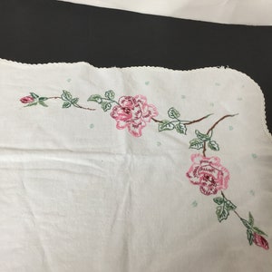 Op de afbeelding: Witte geborduurde tafelloper met roze rozen en groene bladeren. De loper heeft een gegolfde rand.