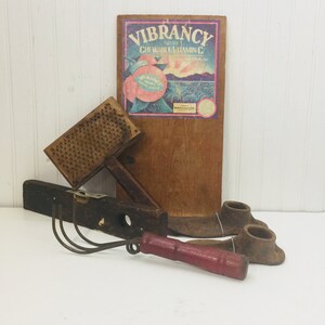 May include: A collection of vintage tools including a wooden grater, a wooden level, a garden rake with a red handle, and two metal shoe lasts. A wooden sign with the text "Vibrancy Frankly Chewable Vitamin C" is also included.