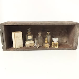 May include: A wooden box with a collection of vintage perfume bottles. The bottles are clear glass with gold accents and some have labels. The box is brown and has a worn look.
